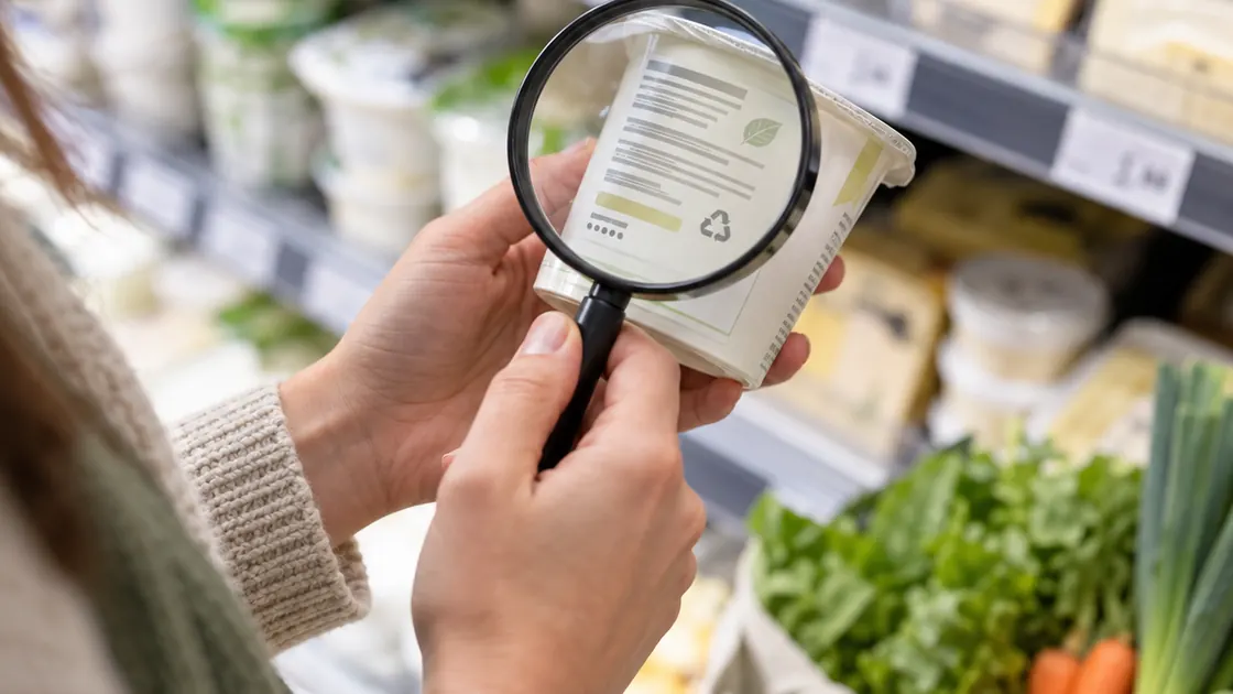 Lebensmittel Schwangerschaft – unmarkierte Milchproduktverpackung wird im Supermarkt mit einer Lupe geprüft.